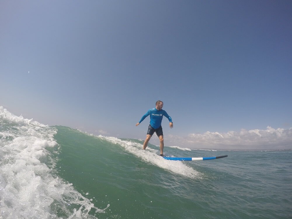 Beginner surfer catching a good wave in Canggu, Bali, after asking a surf school about the best time for a first surf lesson